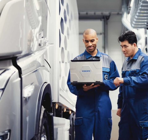 A couple of diesel repair specialists standing next to each other in front of a truck